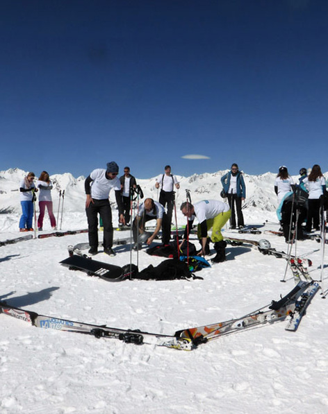 Mehrere junge Menschen legen ihre Skier und Snowboards zusammen als Schnecke in den Schnee