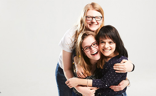 Drei junge Frauen umarmen sich und lachen in die Kamera